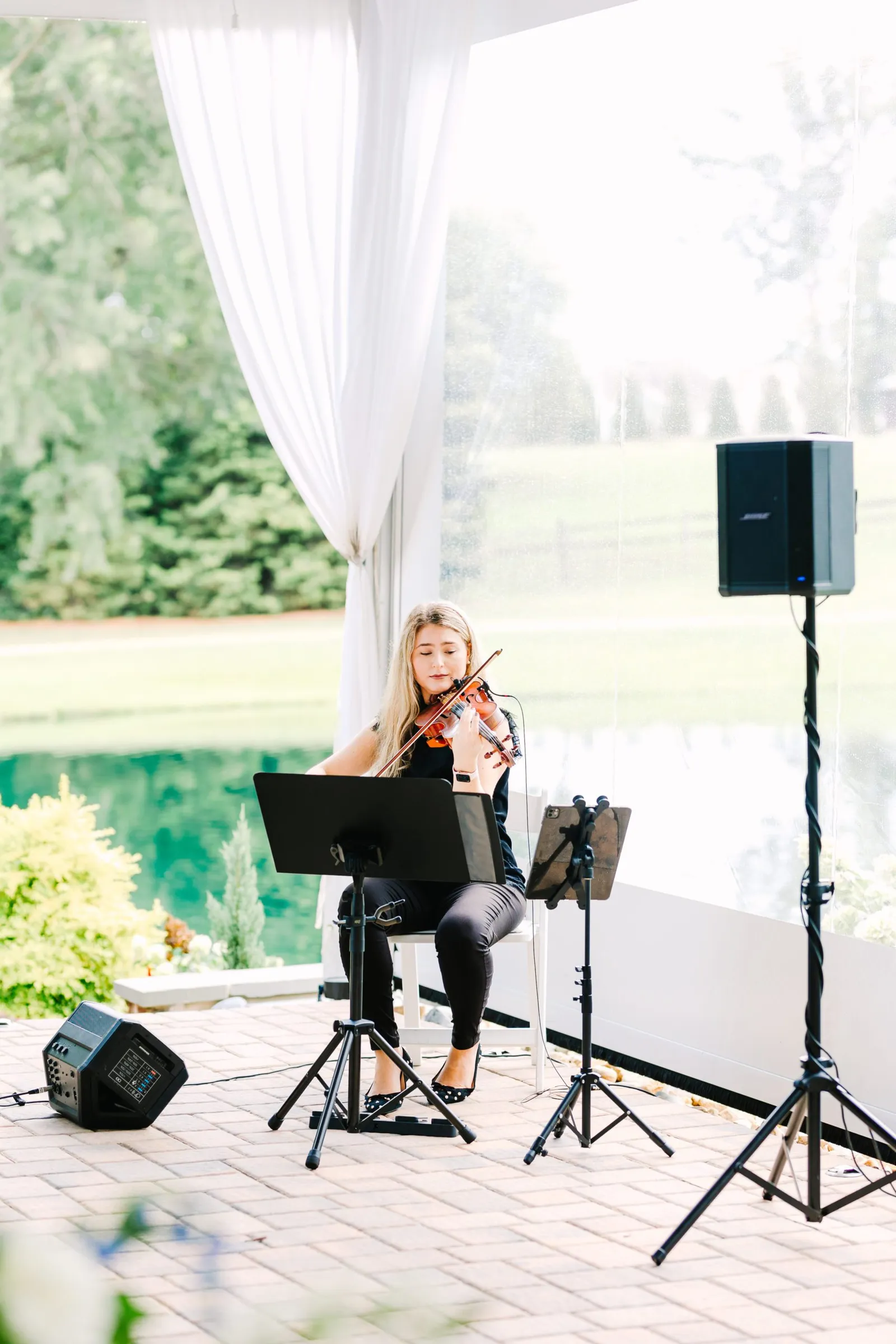 Solo violinist performing beneath a draped tent at a lakeside wedding ceremony