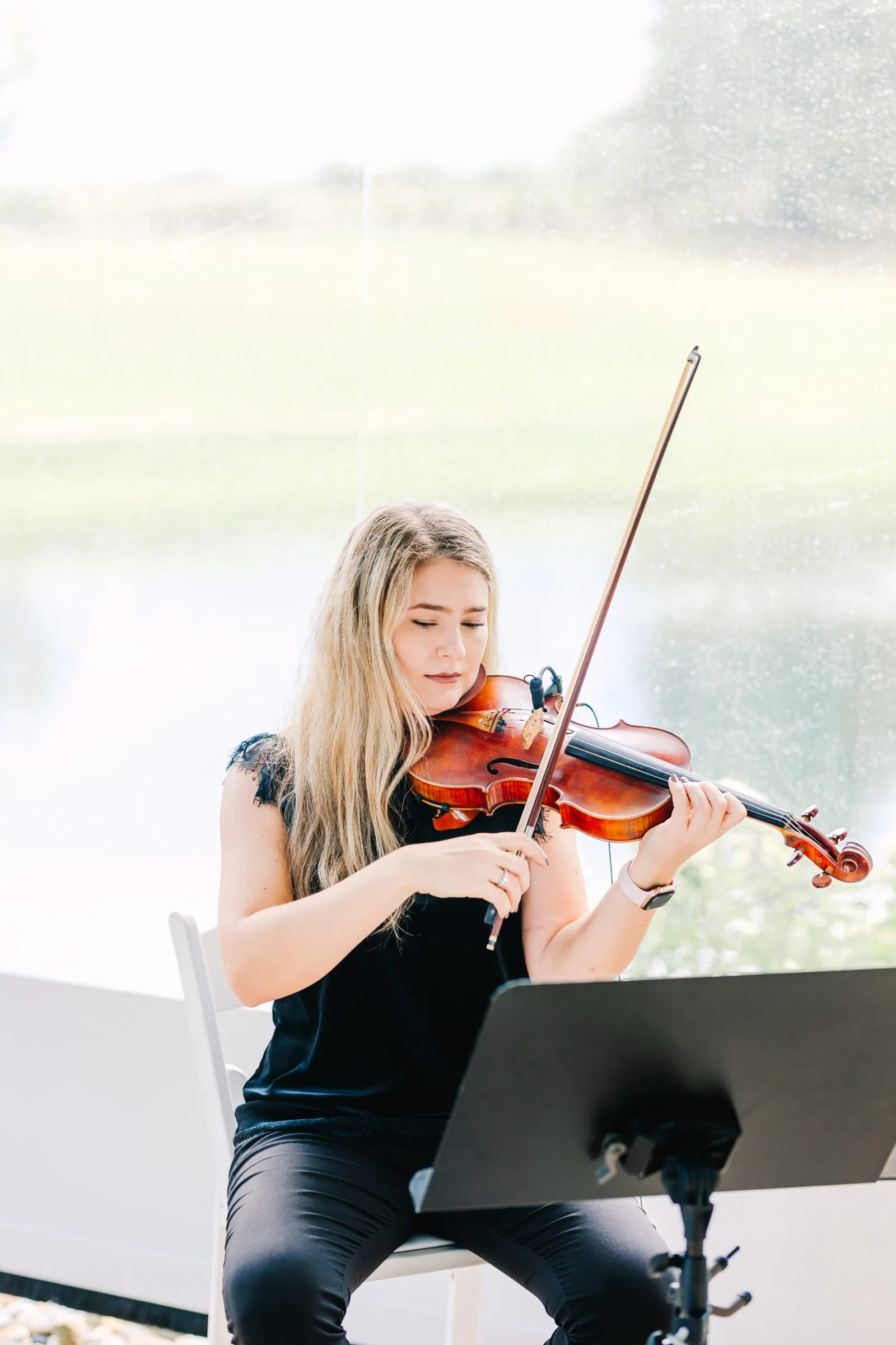 Violinist close-up in luminous backlit wedding tent with focused expression