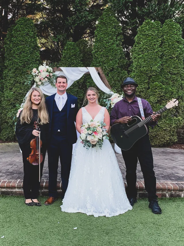 Violin and guitar duo performing at floral arch with joyful wedding group