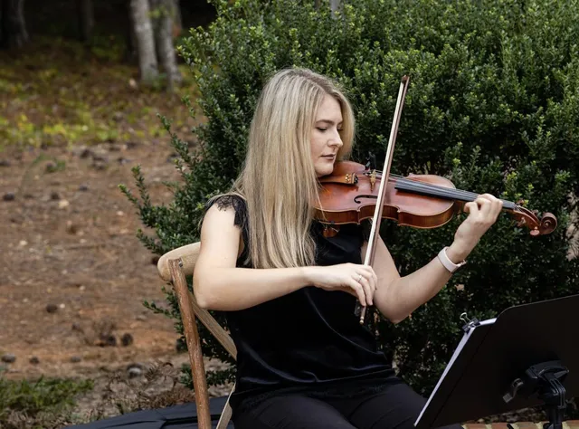 Violinist performing against boxwood hedge in clean garden ceremony setting