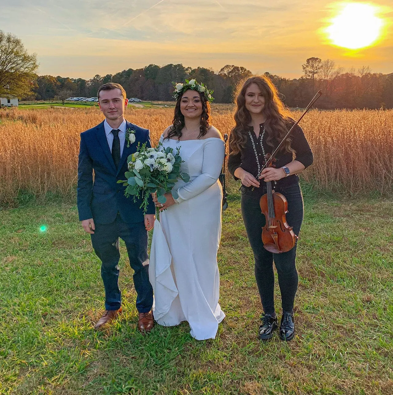 Couple with violinist at golden sunset field backdrop, warm and emotional wedding ceremony