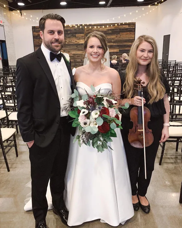 Couple and violinist at modern industrial venue with warm string lights