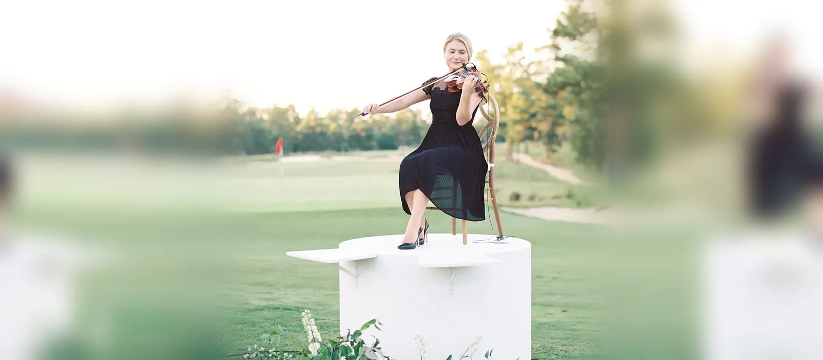 Solo violinist performing on a white pedestal beside a golf green at a Dormie Club wedding in the North Carolina Sandhills