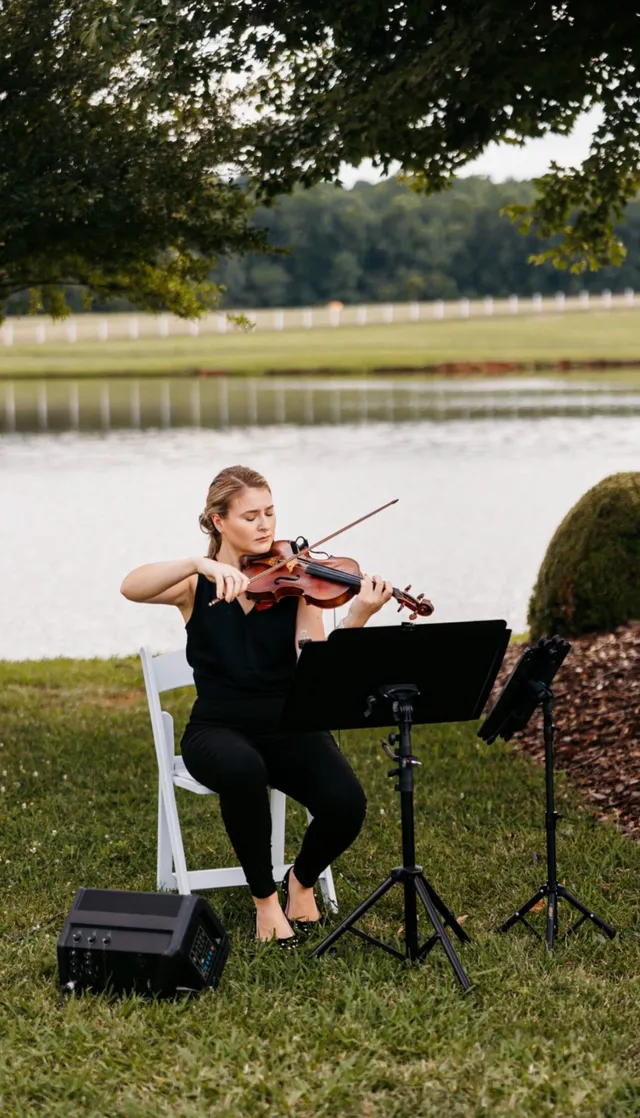Solo violinist performing at dusk on a waterside lawn