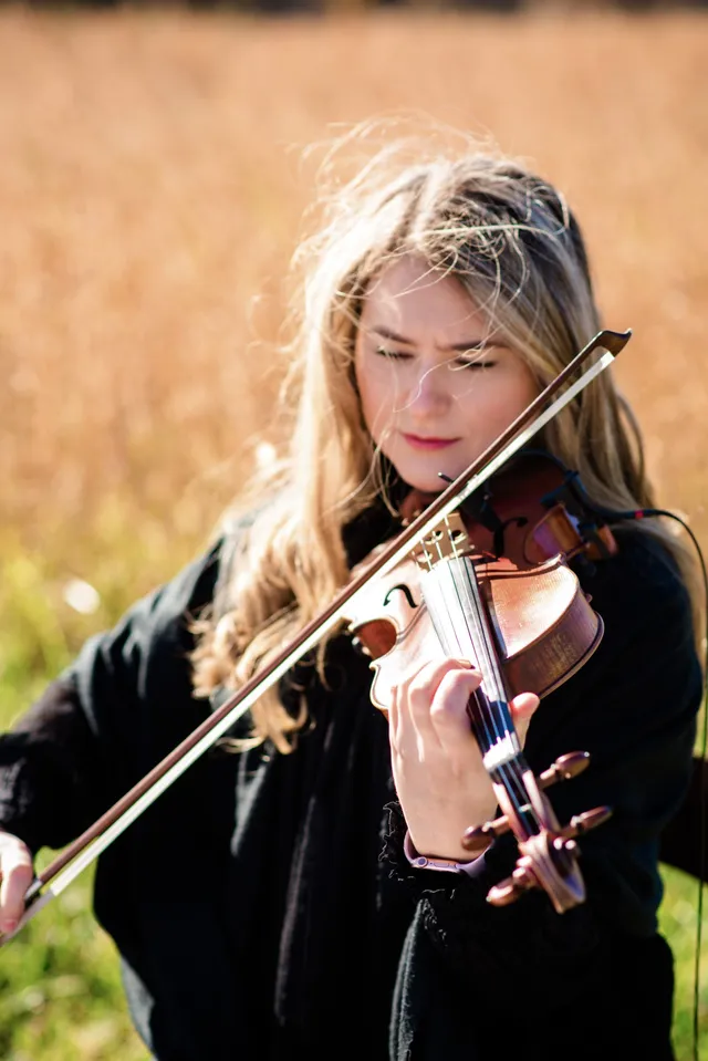 Windswept portrait of violinist playing in a golden field with hair in motion