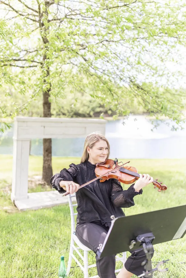 Smiling violinist performing lakeside under a blooming spring tree, warm and approachable