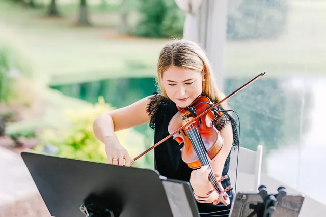 Violinist in lace dress playing outdoors with warm bokeh pool backdrop, focused expression