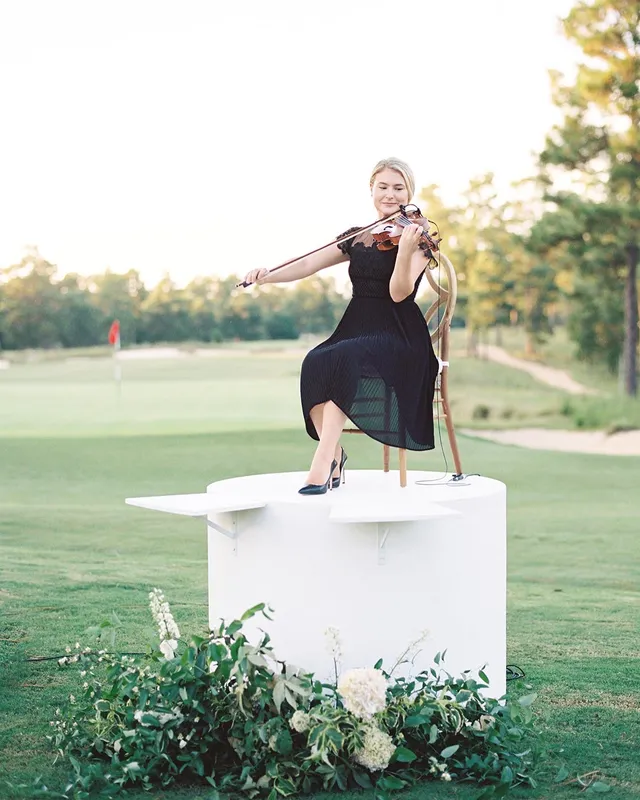 Solo violinist performing on a white pedestal beside a golf green at a Dormie Club wedding