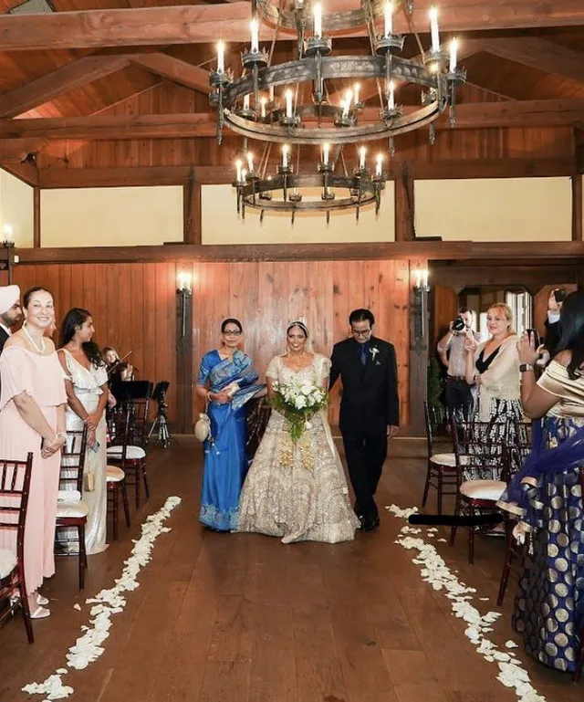 Indian wedding processional in rustic barn with candelabra chandelier, vibrant celebration